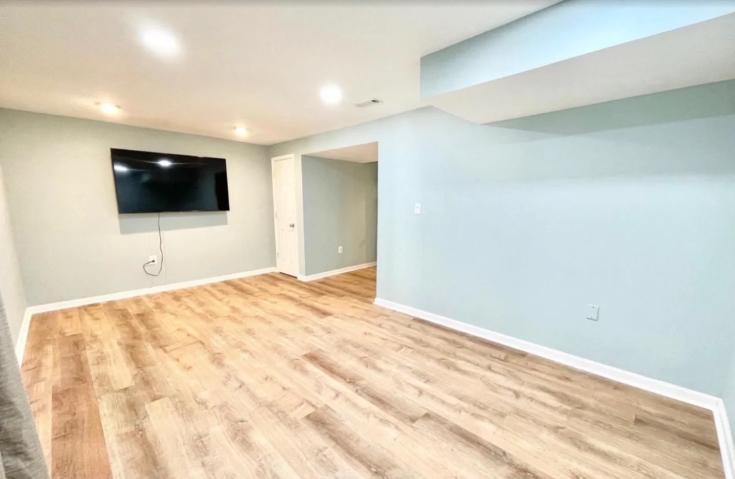 Finished basement room with wood-look flooring and recessed lighting